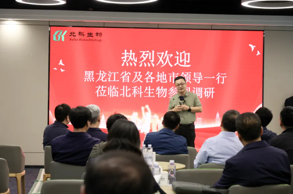 Speaker addressing seated guests in front of a screen welcoming the Heilongjiang delegation