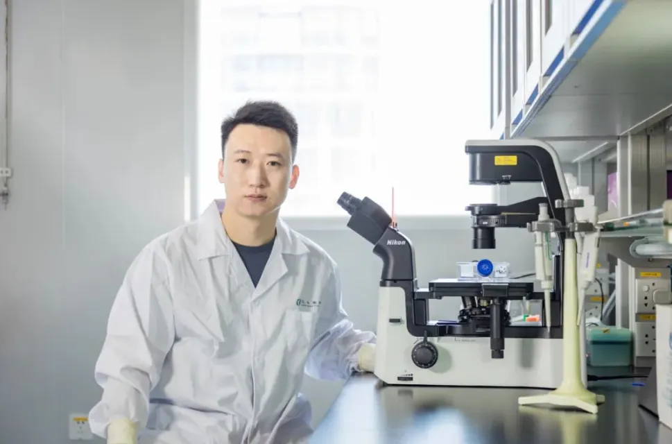 Liao Yan in a lab coat beside an inverted microscope in the Beike Biotech laboratory